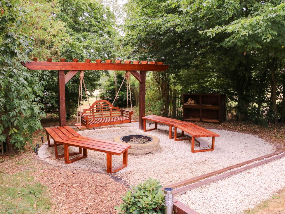 An outdoor area with a swing, wooden benches, fire pit and trees at The Warm Hearth in Hereford