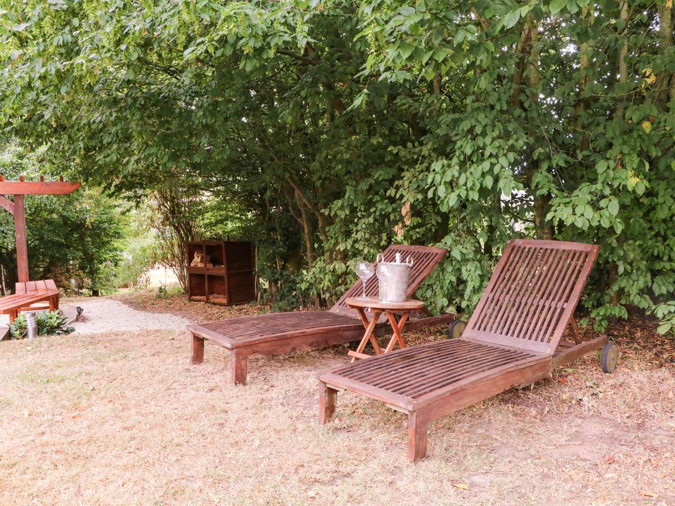 Two wooden deck chairs and a side table in a garden at The Warm Hearth in Hereford