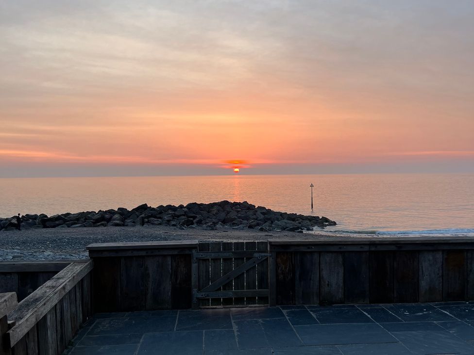 A sunset over the sea with rocks and a gate at Y Glyn in Borth