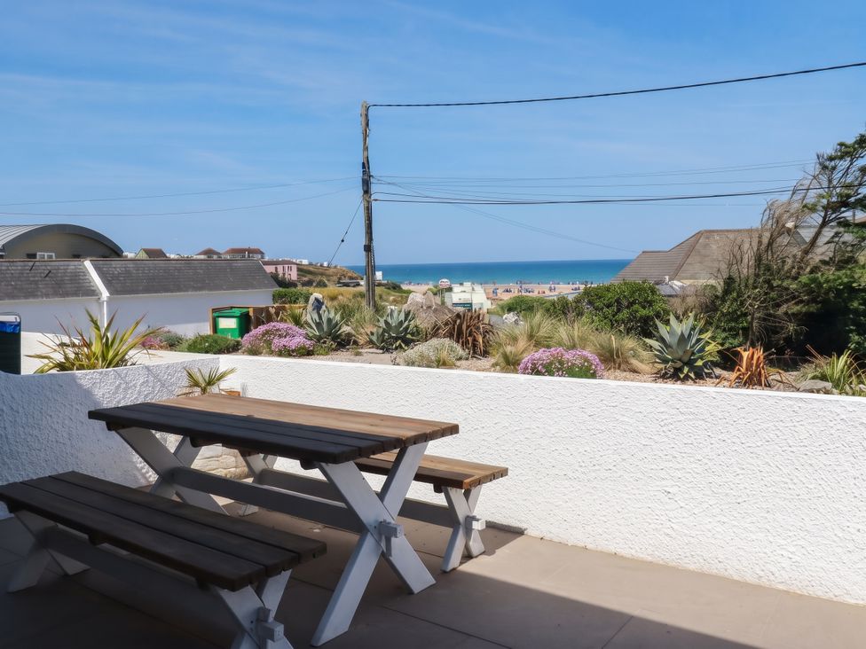 An outdoor seating area with a table and bench overlooking the sea at 9 Tides Reach in Wadebridge