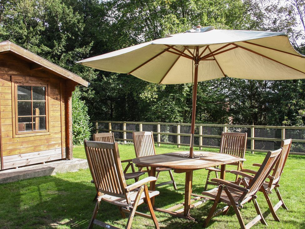 A garden with a wooden table and chairs under a parasol at Tudor Lodge near Belper