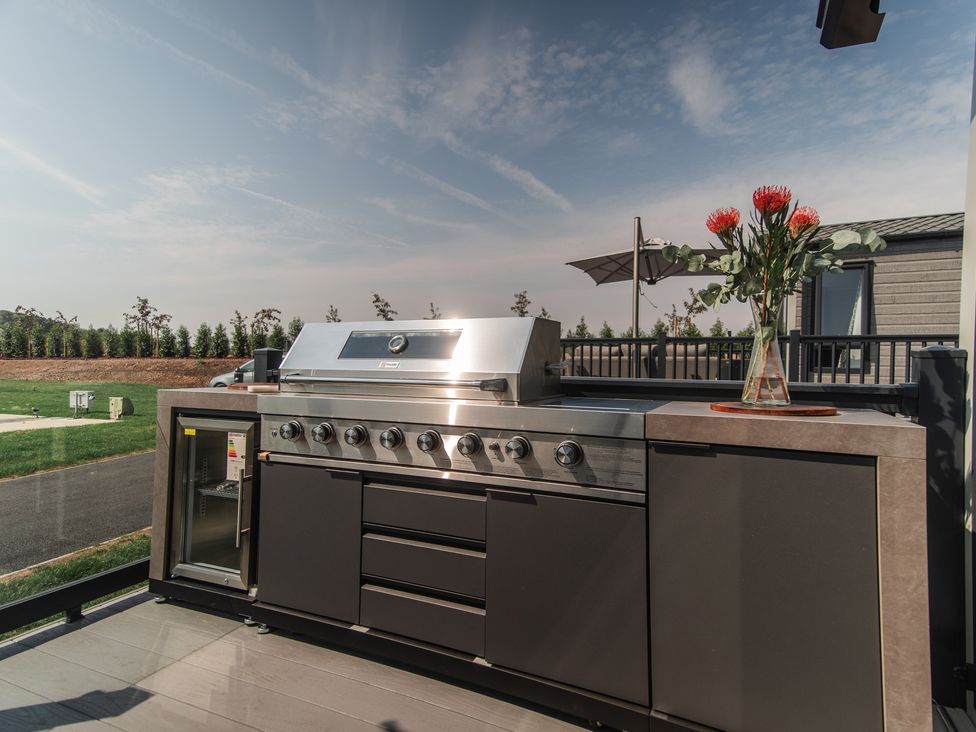 An outdoor kitchen with a grill and a vase of flowers at Lakewood Plot 3 St. Osyth