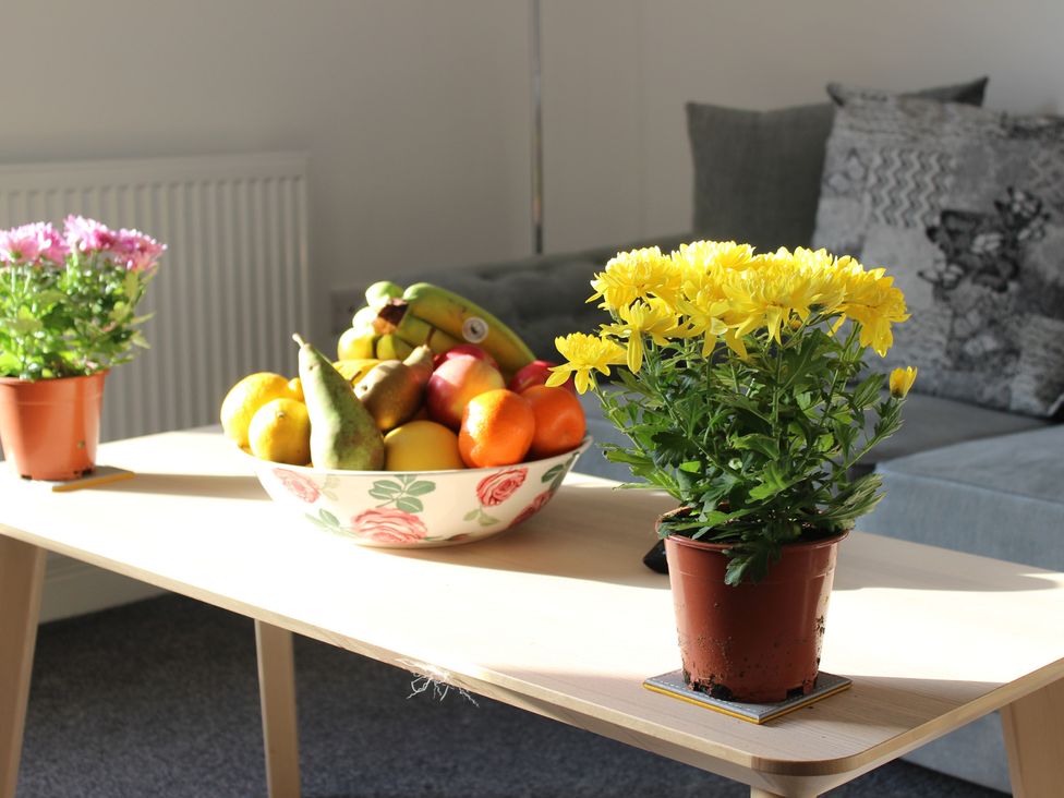 A table with a bowl of fruit and potted plants in a living room at Oliver Wests Apartment 1 Scarborough