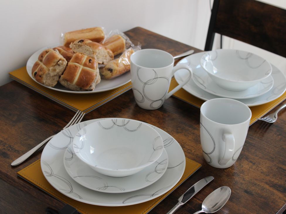 A dining table set with plates, bowls, cups, and bread at Oliver Wests Apartment 1, Scarborough