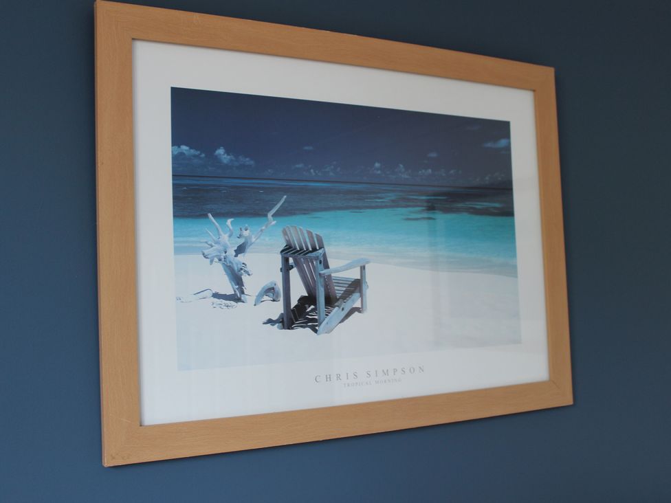 A framed picture of a beach scene with a chair and driftwood at Oliver Wests Apartment 1 Scarborough
