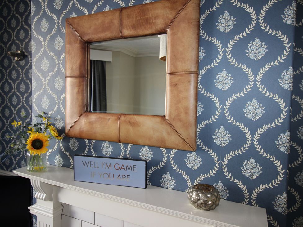 A living room with a mirror, vase with sunflowers, and a decorative sign at The Hampton in Scarborough