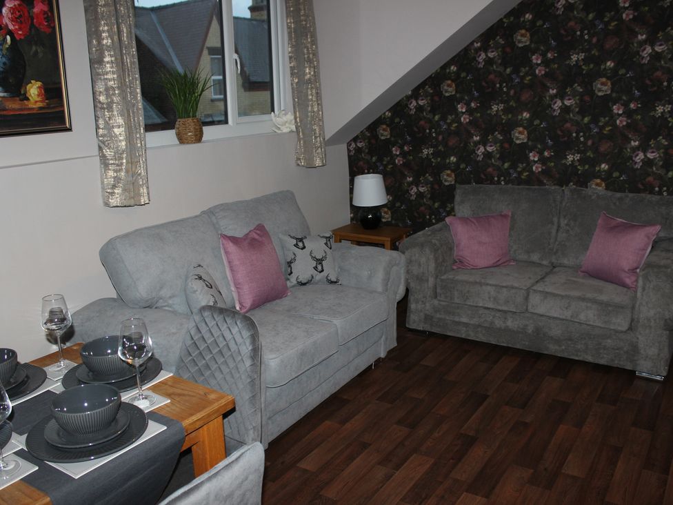 A living room featuring a sofa and armchair with a table set for dining at Blackburn Heights Apartment 3, Bridlington