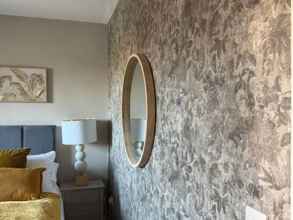 A bedroom with a bed, lamp, nightstand, and mirror at Blackburn Heights Apartment 3, Bridlington