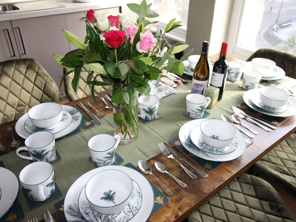 A dining table set with plates, cups, cutlery, and a vase of flowers at Cornerhouse Apartment 1, Llandudno