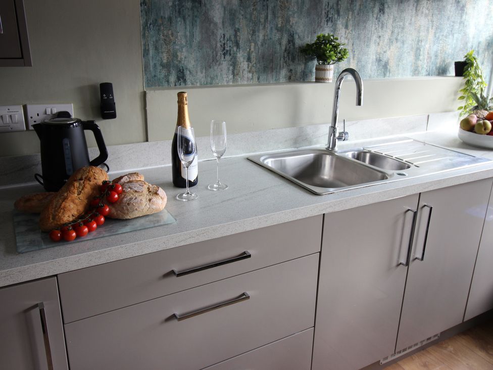 A kitchen with a sink, countertop, kettle, and food items at Cornerhouse Apartment 1, Llandudno