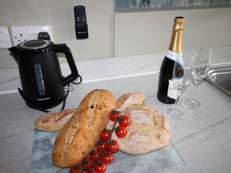 A kitchen with a kettle, champagne, bread, and tomatoes at Cornerhouse Apartment 1 in Llandudno