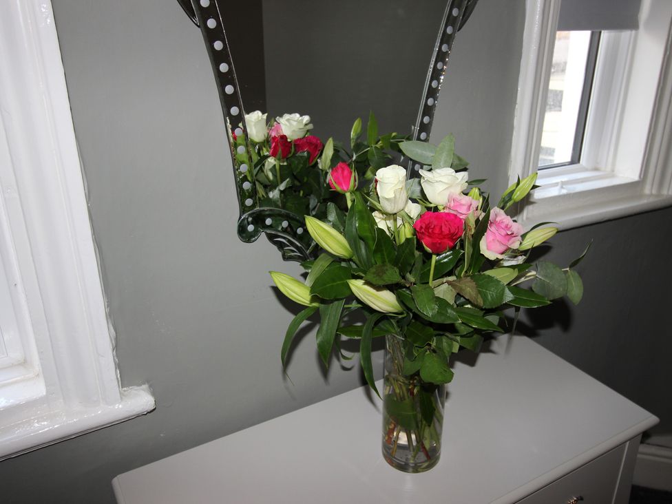 A bouquet of flowers on a table with a mirror in a living room at Cornerhouse Apartment 1 Llandudno