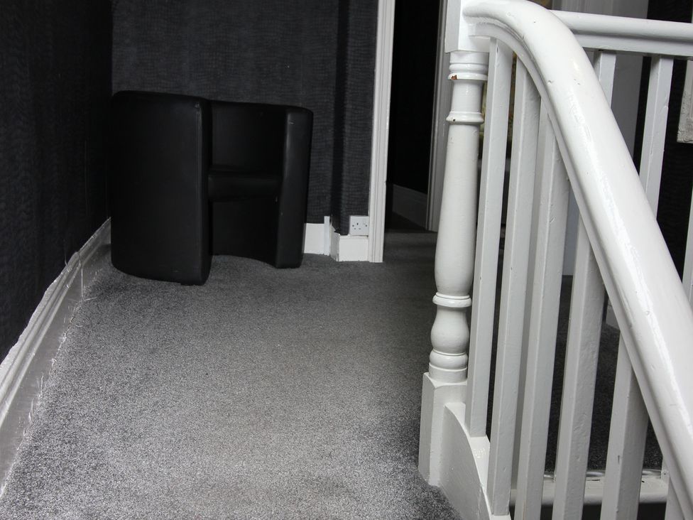 A hallway with a black chair and staircase at Cornerhouse Apartment 1 in Llandudno