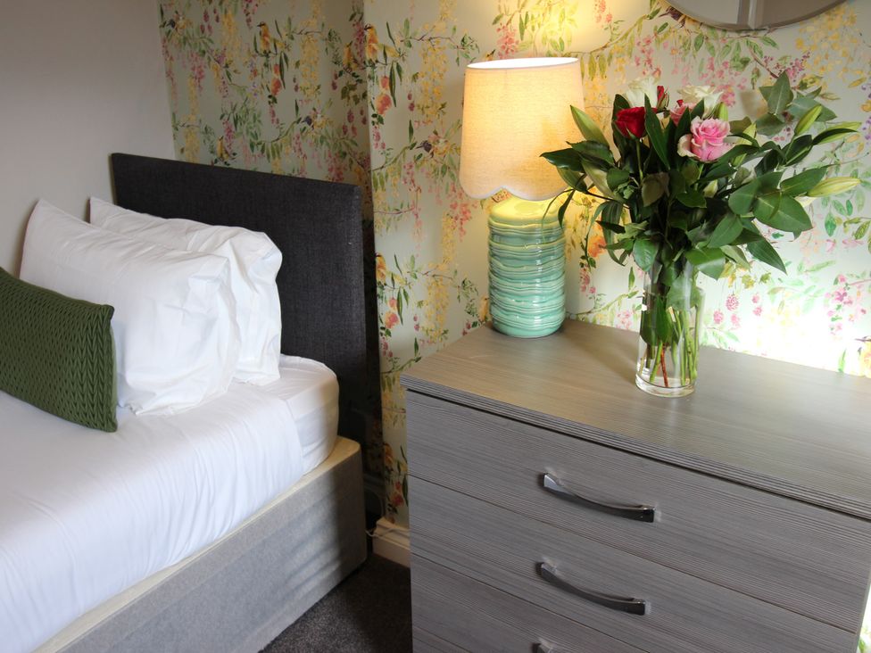 A bedroom with a bed and flowers on a chest of drawers at Cornerhouse Apartment 1 in Llandudno