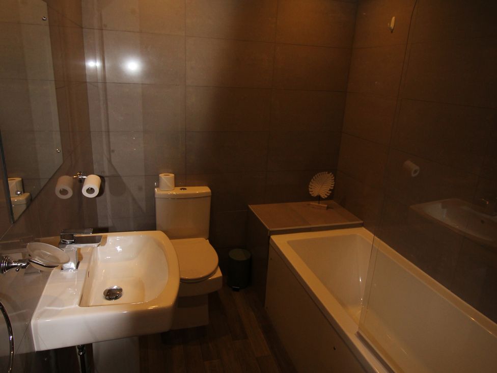 A bathroom with a sink, toilet, bathtub and mirror at Cornerhouse Apartment 1 in Llandudno