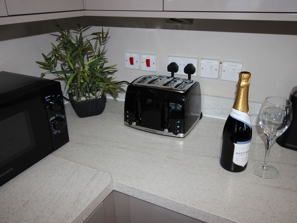 A kitchen counter with a microwave, toaster, plant, bottle, and glass at Cornerhouse Apartment 2 Llandudno