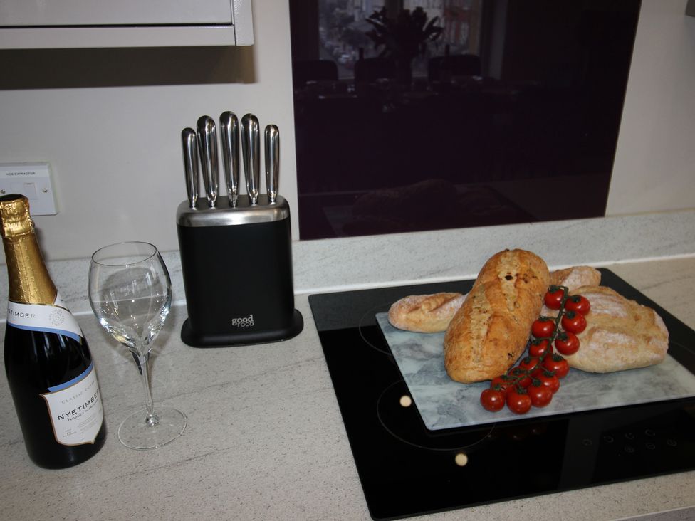 A kitchen with a wine bottle, glass, knife block, bread, and cherry tomatoes at Cornerhouse Apartment 2 Llandudno