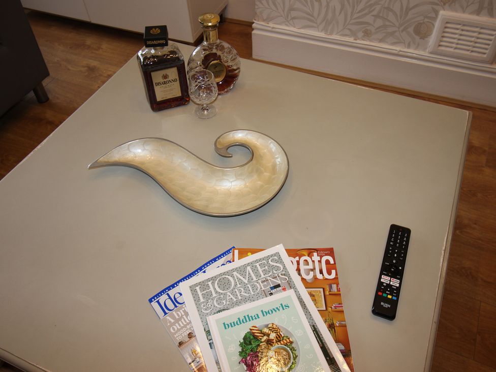 A coffee table with a bowl, magazines, a bottle of liqueur, and a remote control at Cornerhouse Apartment 3 Llandudno