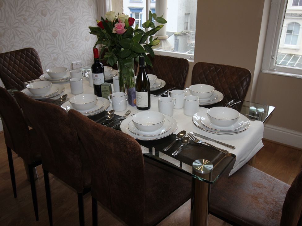 A dining table set with plates, cutlery, and a flower arrangement at Cornerhouse Apartment 3 in Llandudno