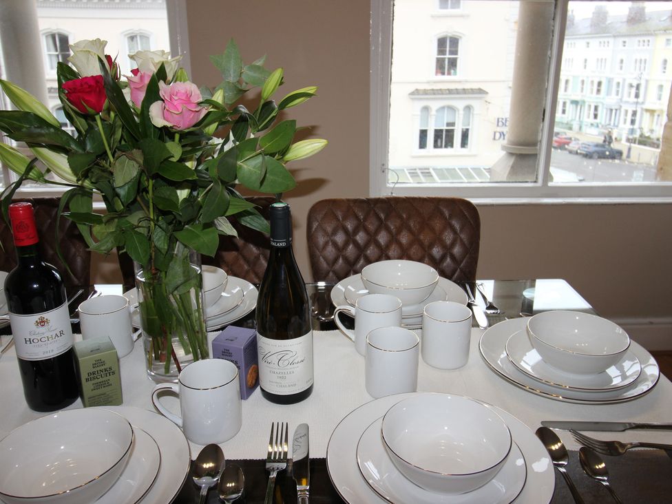 A dining table set with dinnerware and wine bottles at Cornerhouse Apartment 3 in Llandudno