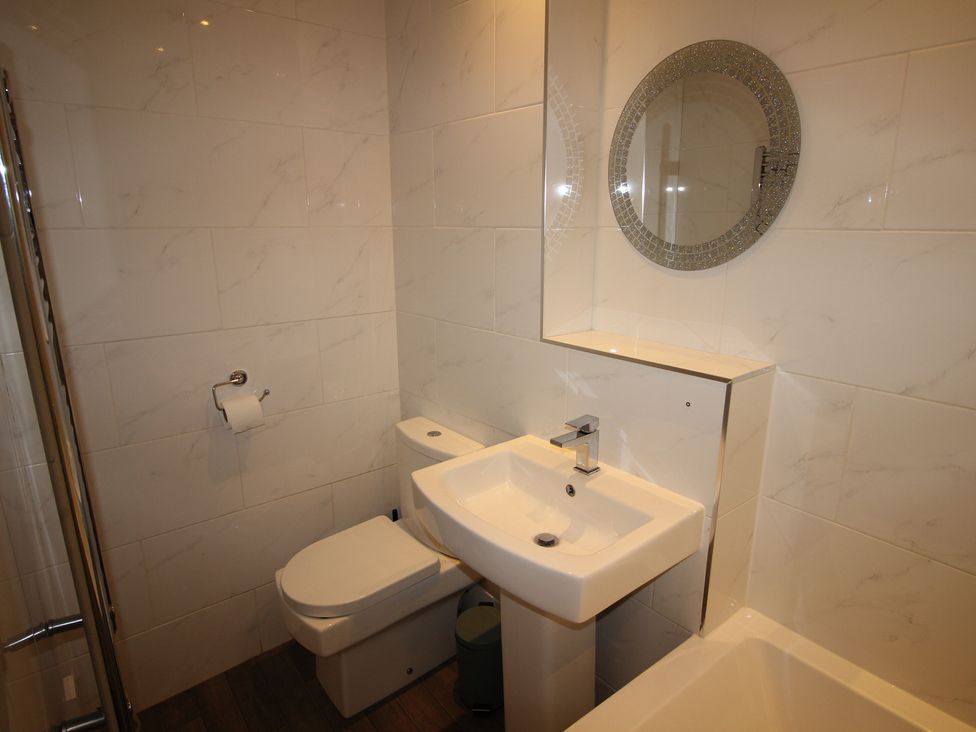A bathroom with a toilet, sink, and mirror at Cornerhouse Apartment 3 Llandudno