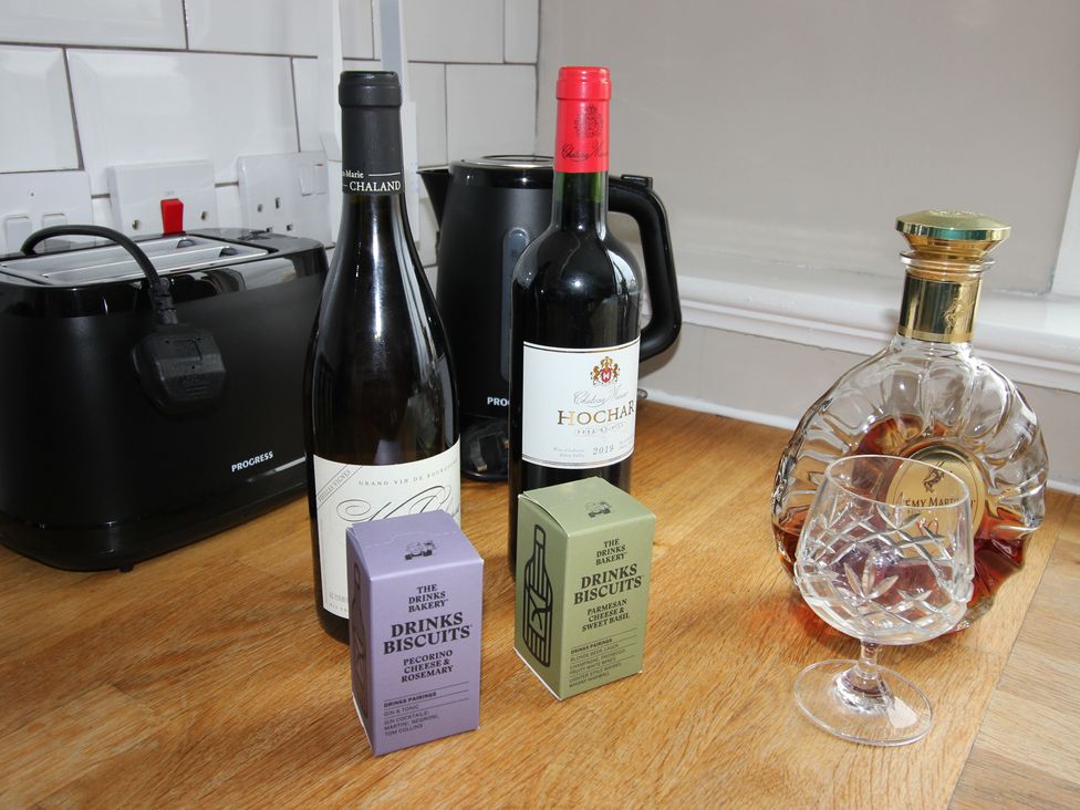 A kitchen with a toaster, wine bottles, a glass, and cheese biscuits at Cornerhouse Apartment 4 in Llandudno