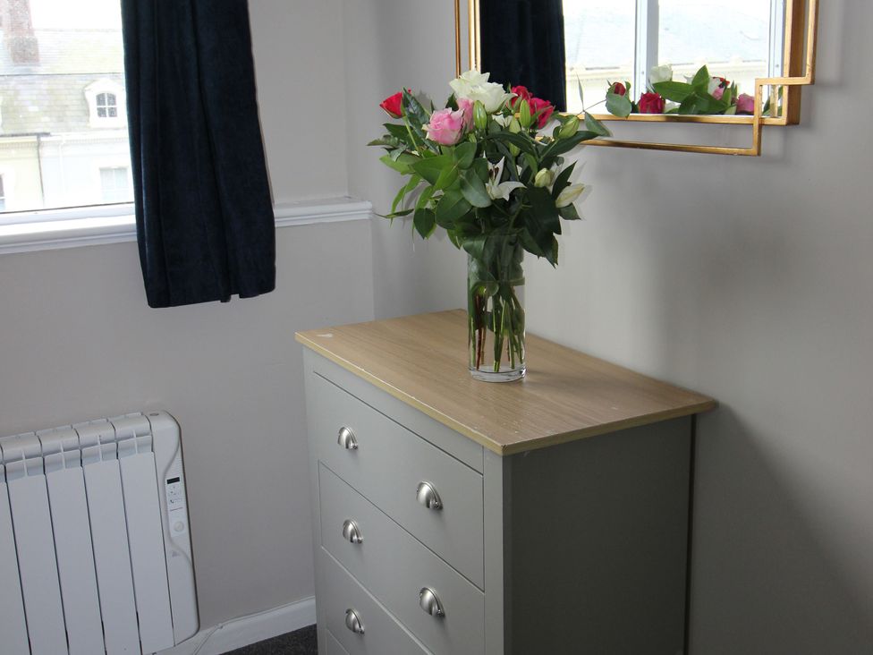 A dressing table with a mirror and flowers at Cornerhouse Apartment 4 Llandudno