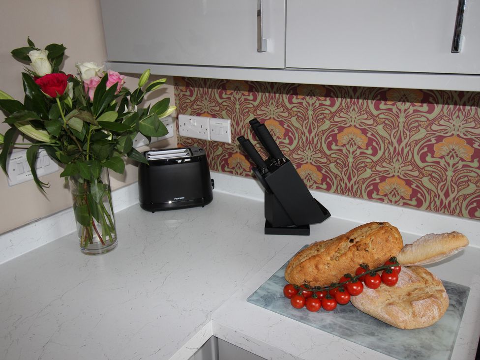 A kitchen with flowers, a toaster, knife block, bread, and tomatoes at Cornerhouse Apartment 5 Llandudno