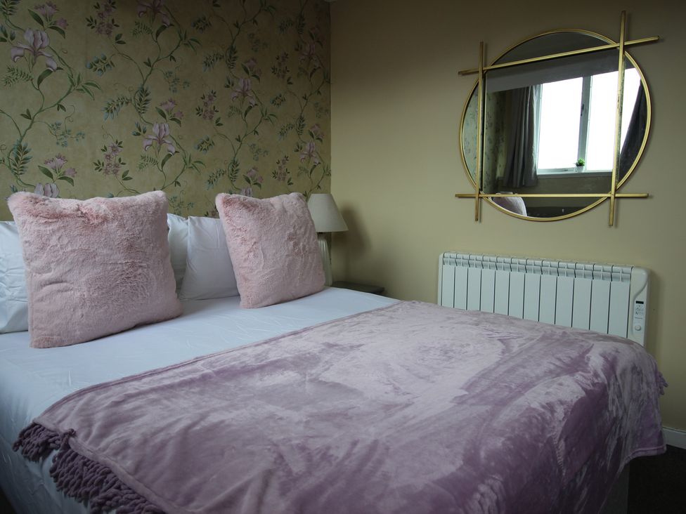 A bedroom with a bed, pillows, lamp, and mirror at Cornerhouse Apartment 5 in Llandudno