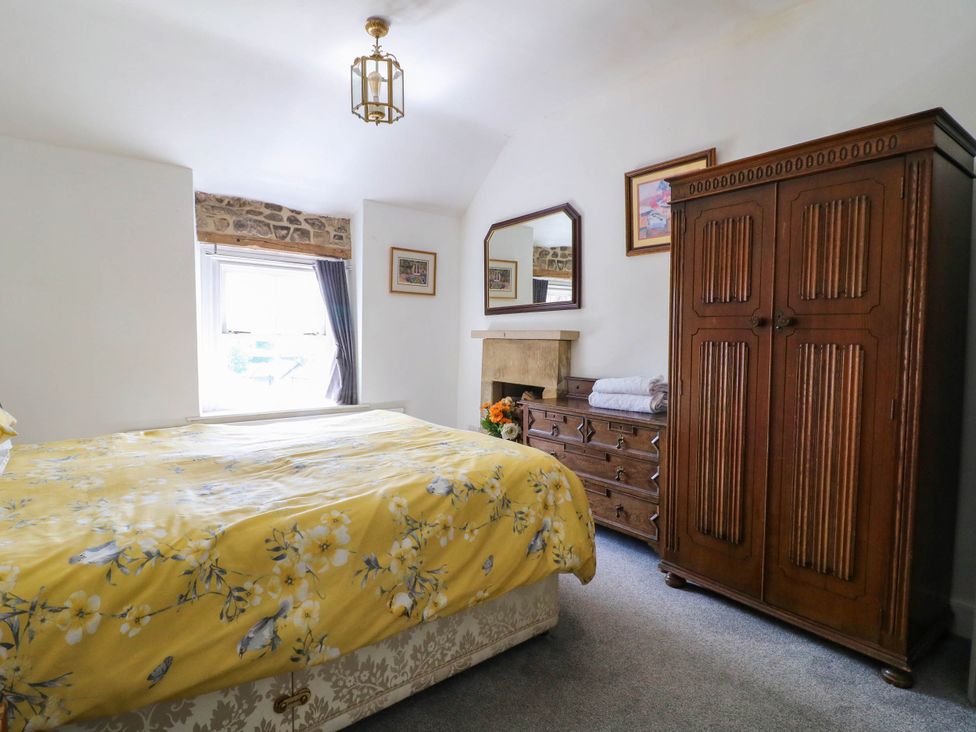 A bedroom featuring a bed with a yellow duvet and vintage wooden furniture at Jasmine Cottage in Matlock