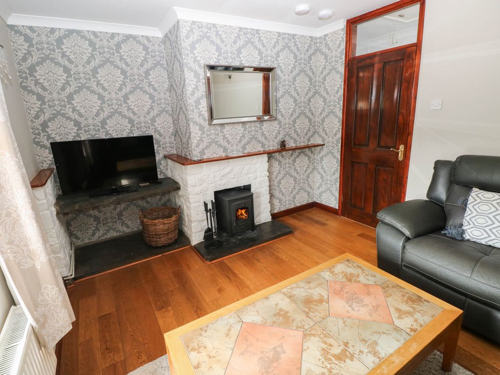 A living room with a TV, sofa, fireplace, and coffee table at Coedllys Uchaf Cottage