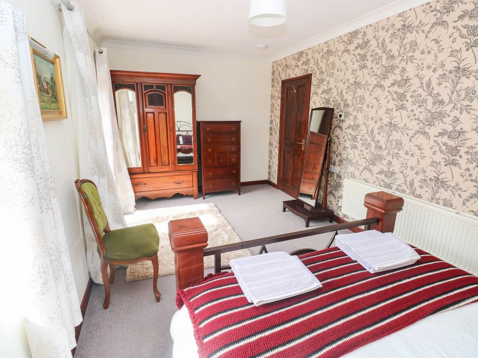A bedroom with furniture including a bed, wardrobe, and chest of drawers at Coedllys Uchaf Cottage