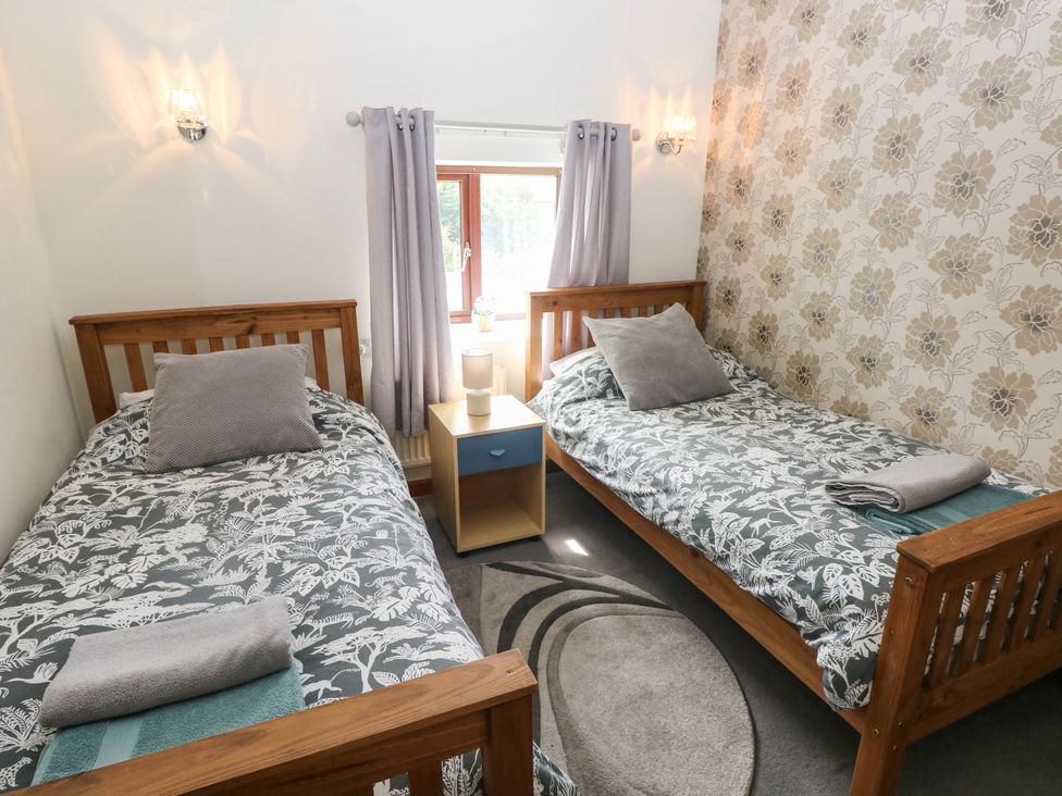 A bedroom with two beds and a side table at Coedllys Uchaf Cottage
