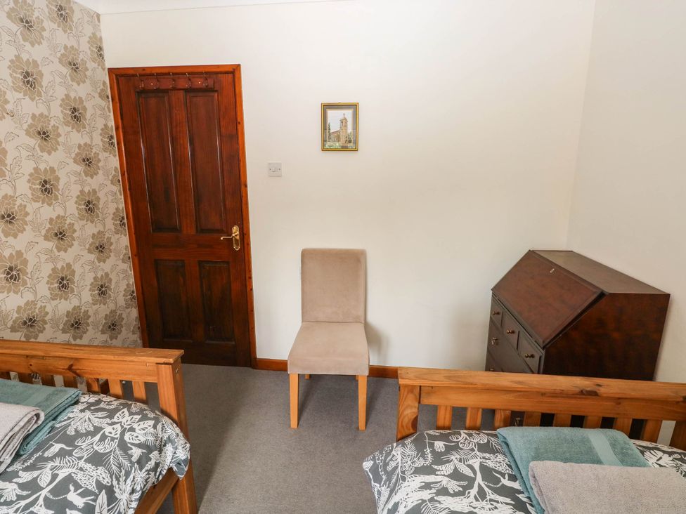 A bedroom with two beds, a chair, a door, and a cabinet at Coedllys Uchaf Cottage