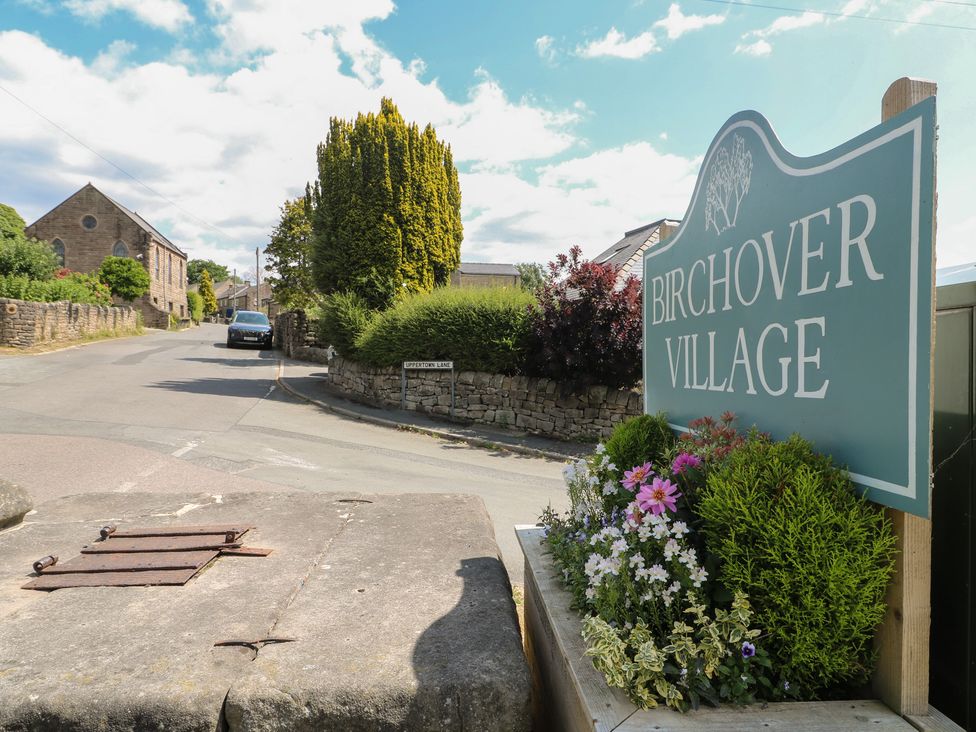 A sign for Birchover Village with flowers at the entrance to the village in Matlock