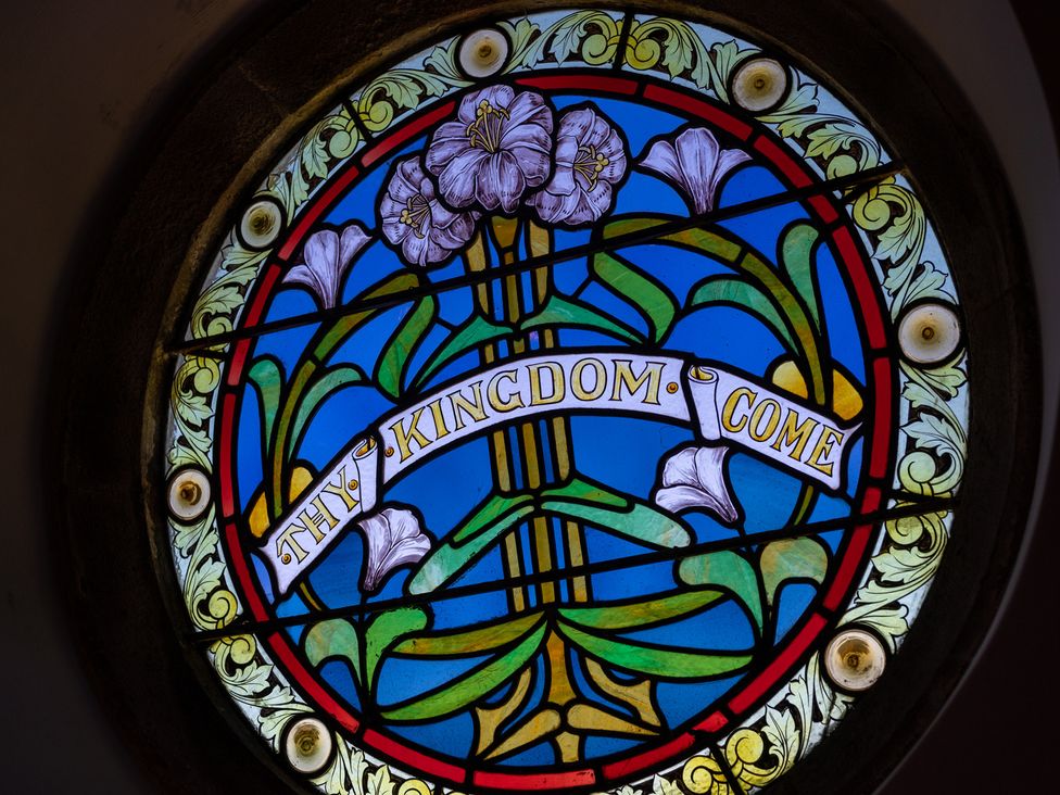 A stained glass window with flowers and text at Birchover Chapel in Birchover