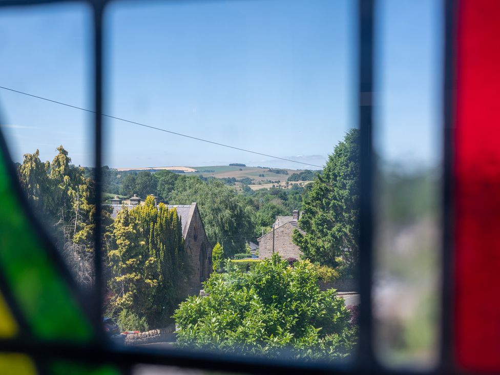 A view through a stained glass window showing trees and houses at Birchover Chapel, Birchover