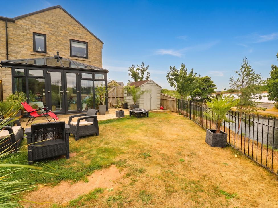A garden with a glass conservatory and seating area at Canal House in Shipley