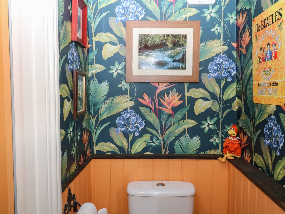 A bathroom with a toilet, framed artwork, and floral wallpaper at Little Moorgate in Okehampton