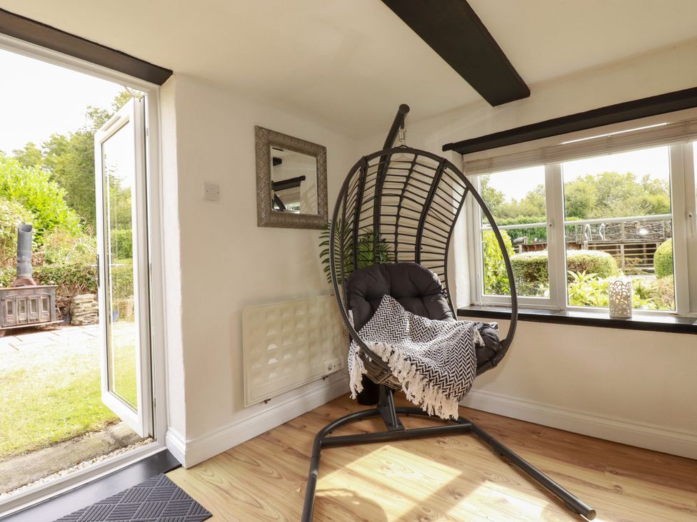 A room with a hanging chair and window at Honey Bee Cottage in Menheniot