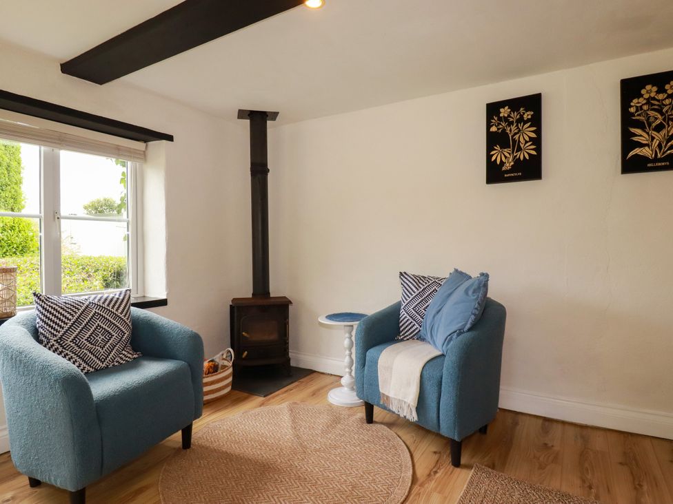 A snug with armchairs and a wood stove at Honey Bee Cottage Menheniot