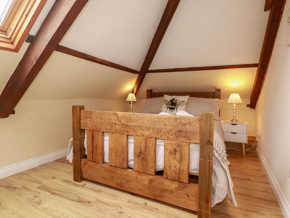 A bedroom with a wooden bed and nightstand at Honey Bee Cottage in Menheniot