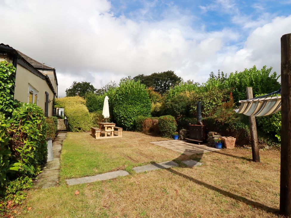 A garden with a table, umbrella, and grill at Honey Bee Cottage in Menheniot