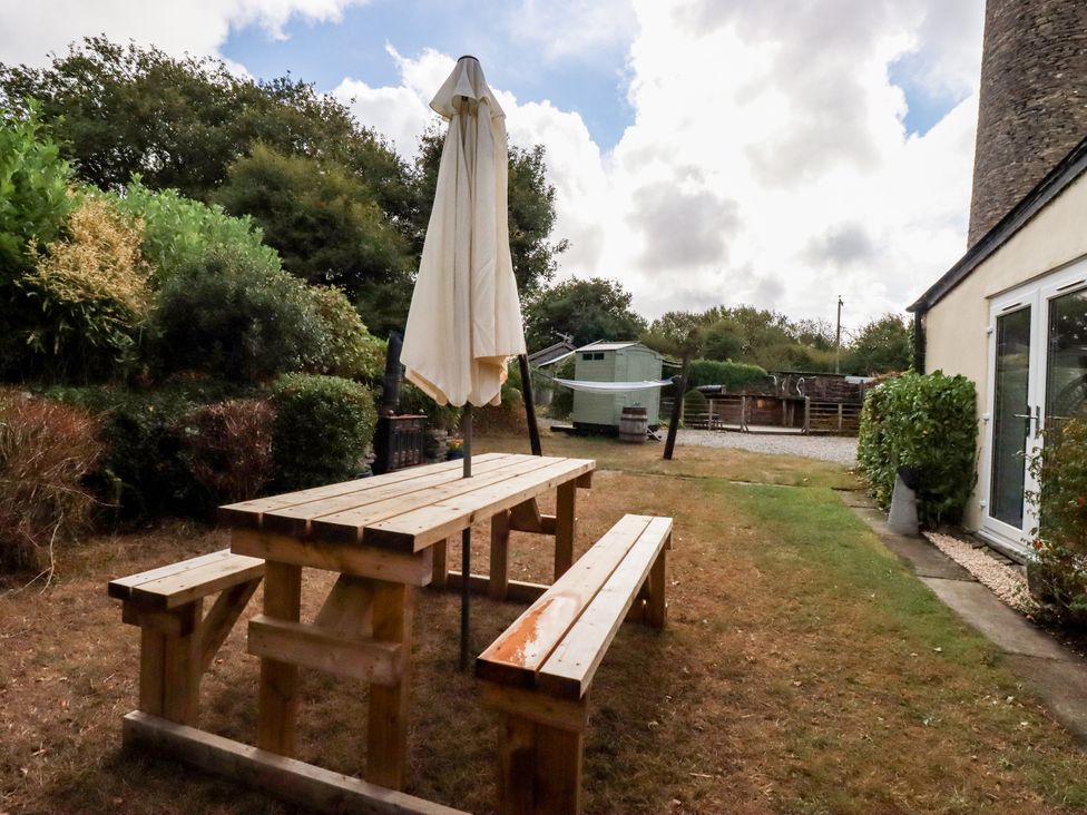 A garden with a table and benches under an umbrella at Honey Bee Cottage in Menheniot