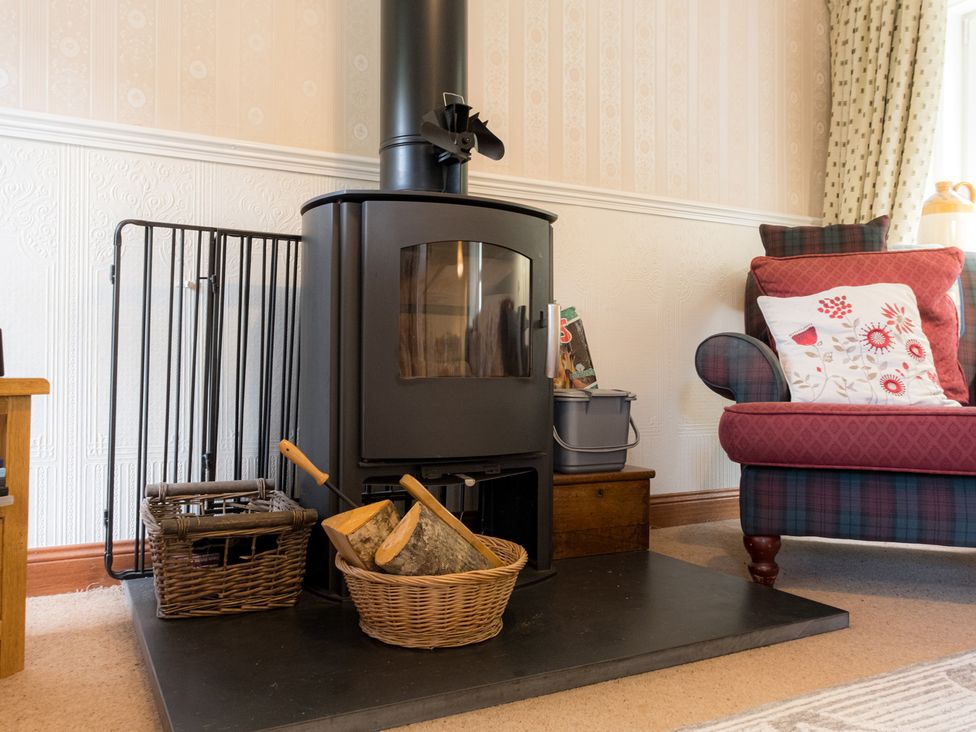 A living room with a wood stove and armchair at Curlew Cottage in Crianlarich