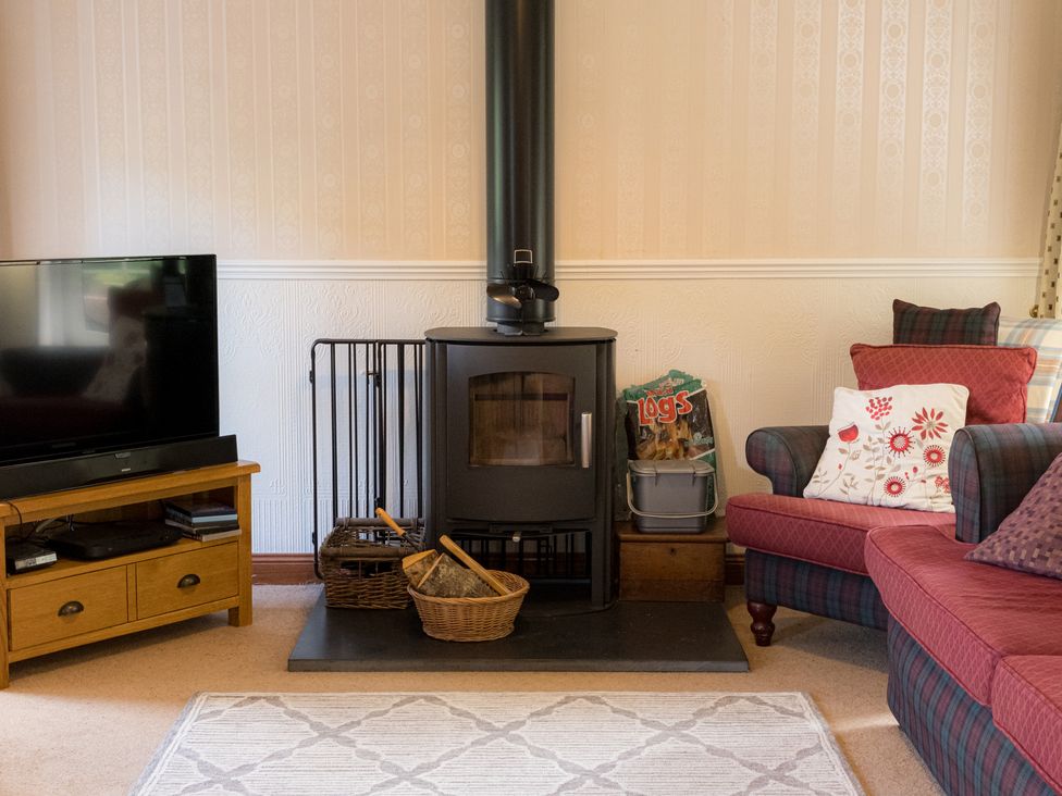 A living room with a wood stove and television at Curlew Cottage in Crianlarich