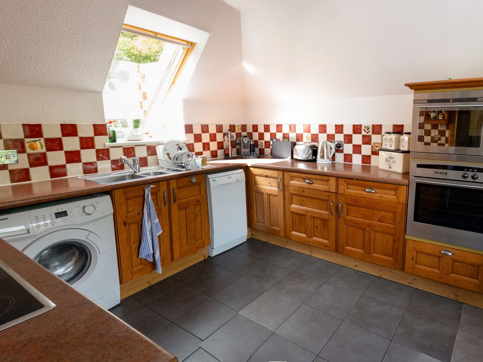 A kitchen with appliances and wooden cabinets at Curlew Cottage in Crianlarich