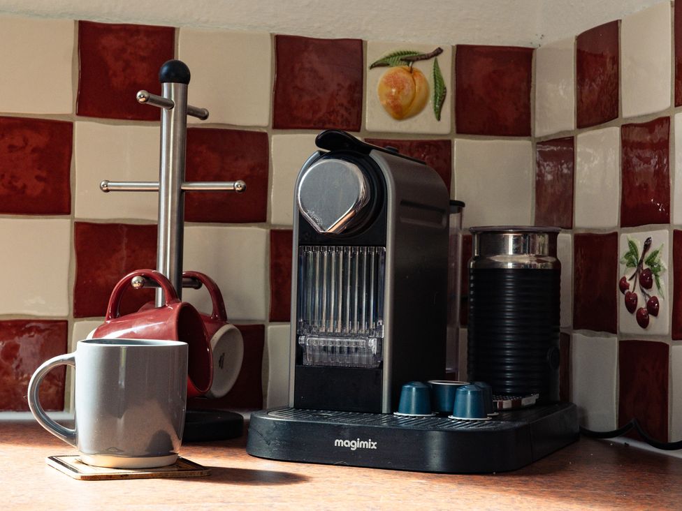 A coffee machine with a mug and milk frother at Curlew Cottage in Crianlarich