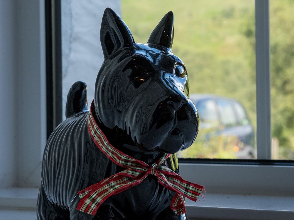 A dog figurine with a ribbon near a window at Curlew Cottage Crianlarich