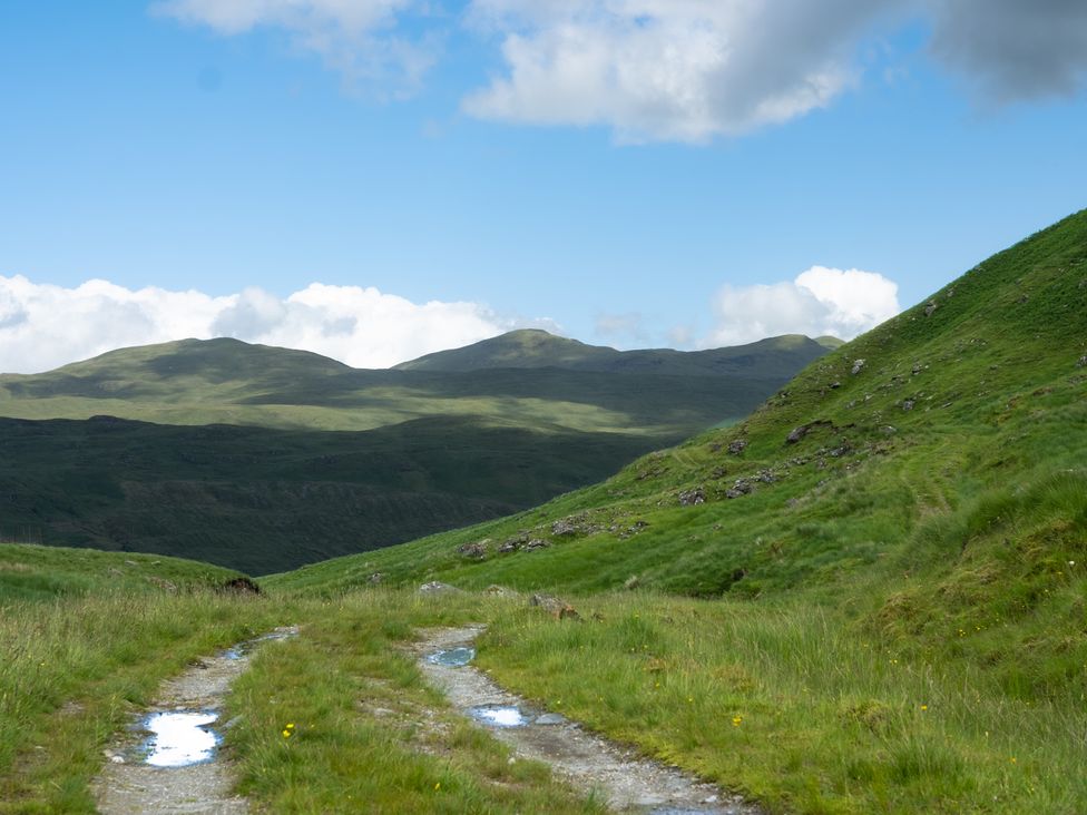 A road surrounded by grass and mountains at Curlew Cottage Crianlarich